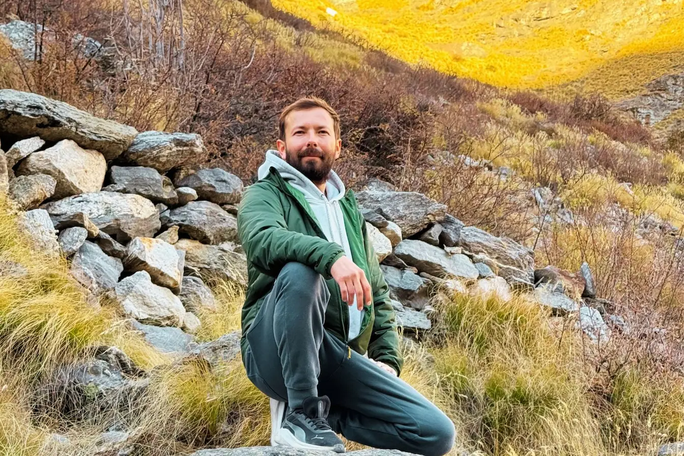 Retreat and Wellness Coordinator Dinesh sitting outdoors on mountain rocks during a nature hike.