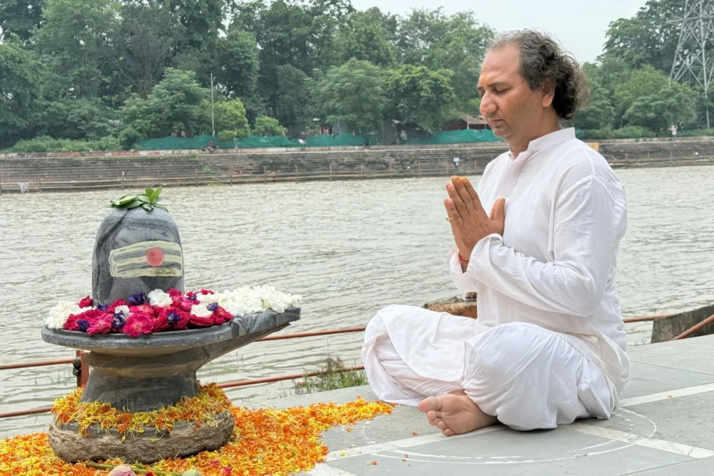 Person meditating in front of a decorated Shiva Lingam by the riverside.